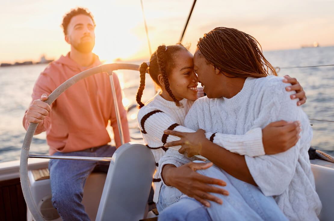 Father sailing the yacht while mother and daughter embrace and enjoy the view. Luxury vacation at sea.